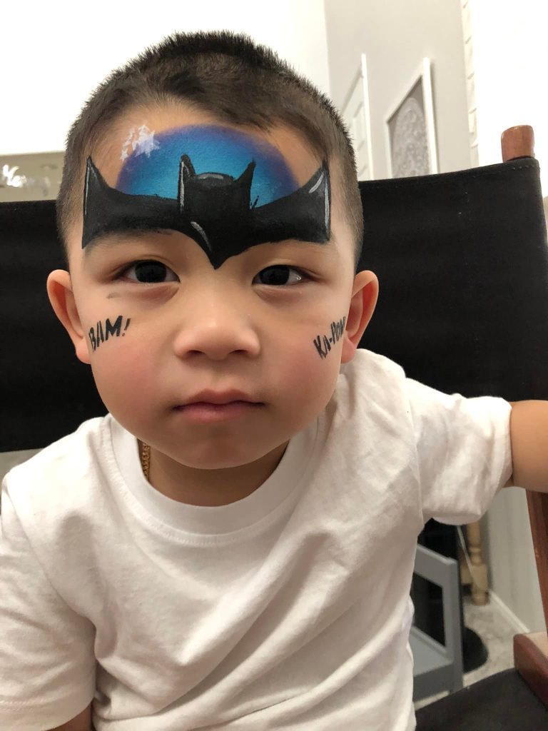 Child showing symmetrical black and blue superhero face paint