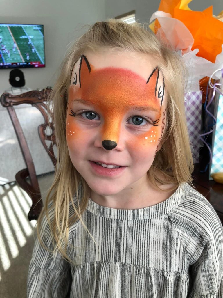 Child smiling with orange fox face painting at a Sparkles the Clown event