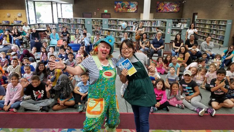 Sparkles and a library host posing with a large audience of children and families