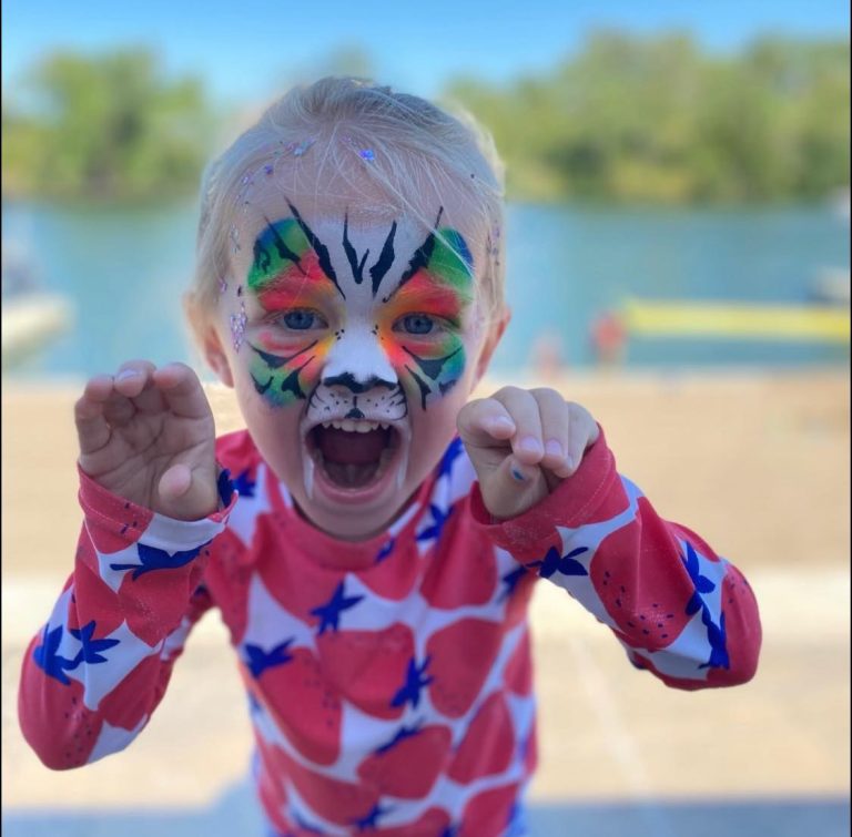 Child roaring playfully with vivid red and blue superhero face and body painting
