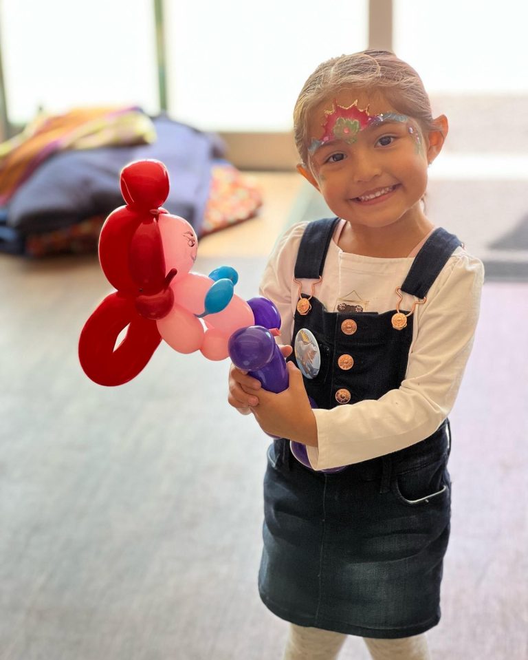 Child smiling while holding a red and purple balloon creation