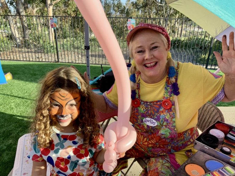 Sparkles posing with a child wearing tiger face paint and holding a pink balloon