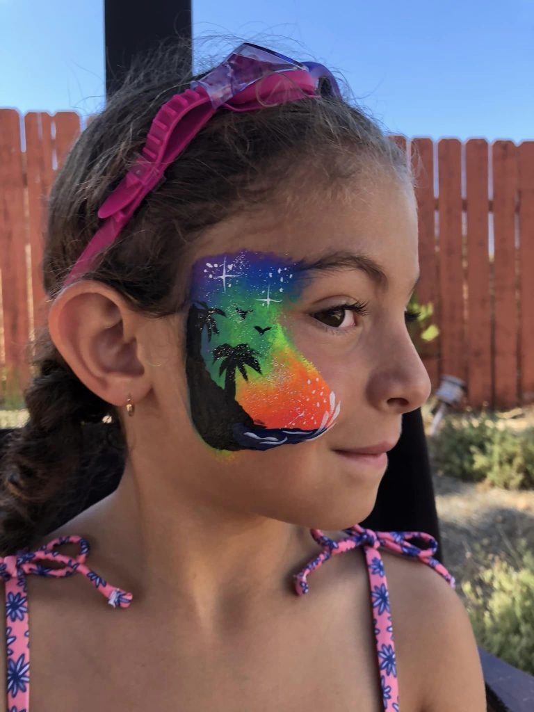 Child showing colorful sunset and palm tree face painting
