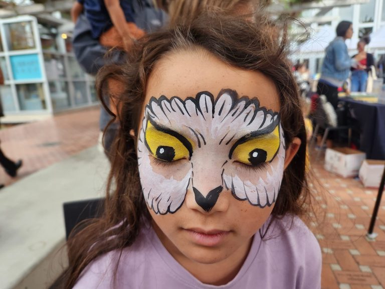 Close-up of detailed white owl face painting with yellow eyes